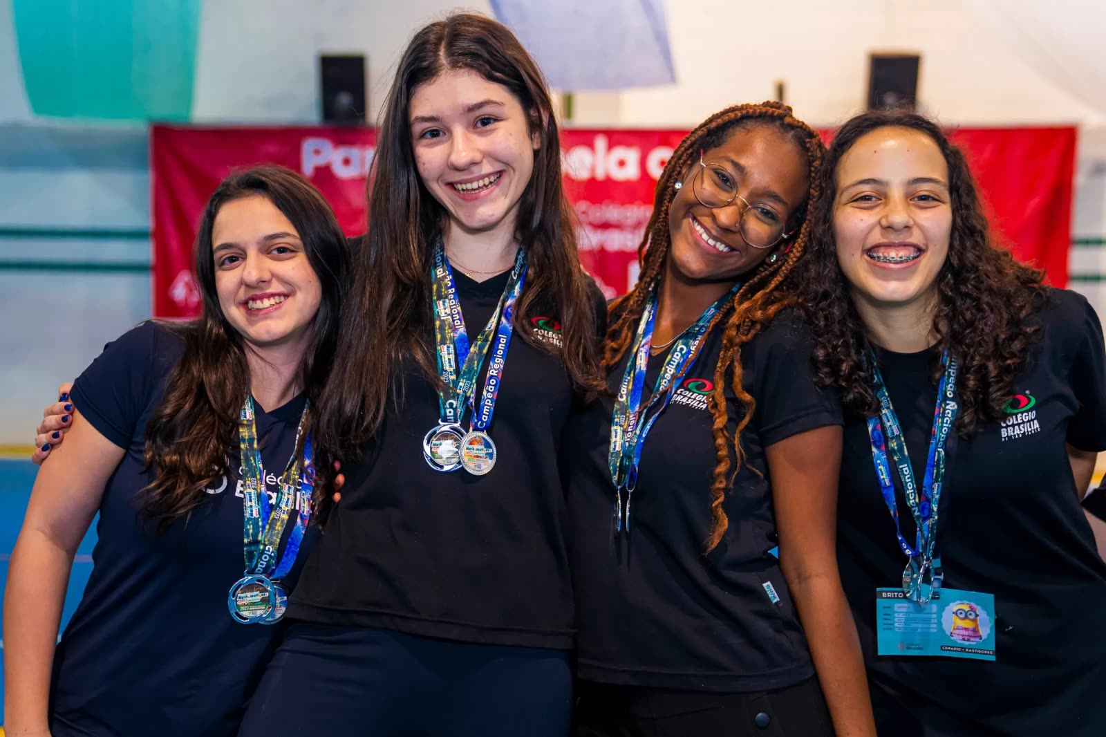 Quatro estudantes sorrindo, medalhas no peito, comemorando juntas